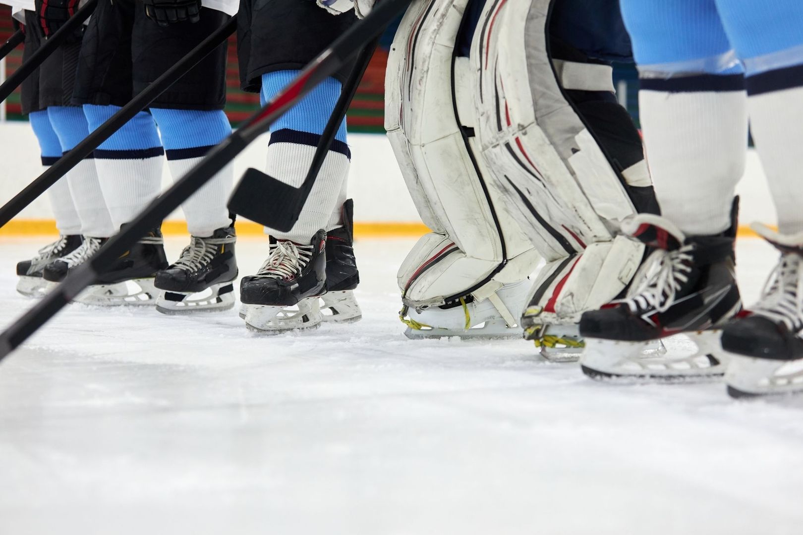 Hockeyspelare på isen med skridskor och klubbor i förgrunden